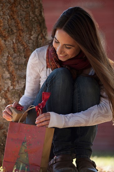 Woman opening gift bag and finding small wrapped gift. Photo : Noah Clayton