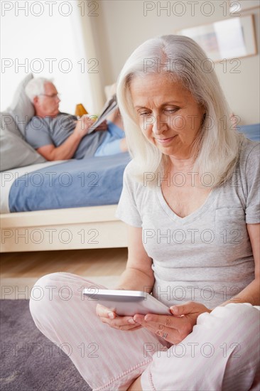 Senior woman holding photo frame, man sitting on bed in background. Photo : Rob Lewine