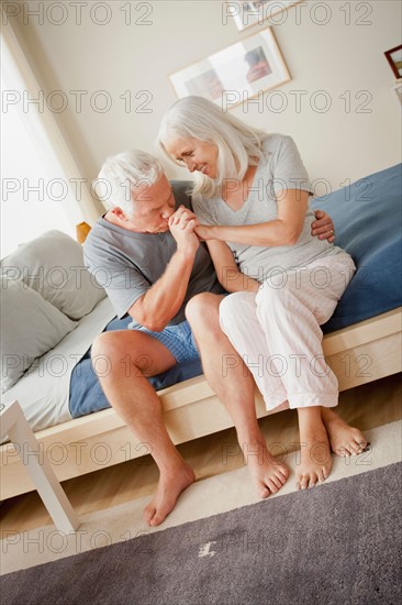 Senior couple sitting on bed in close embrace. Photo : Rob Lewine