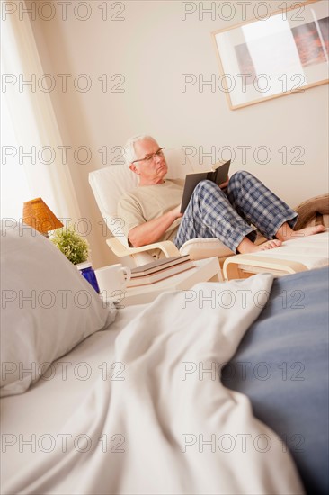 Senior man sitting in bedroom and reading book. Photo : Rob Lewine