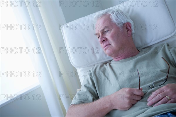 Portrait of senior man holding glasses and thinking. Photo : Rob Lewine