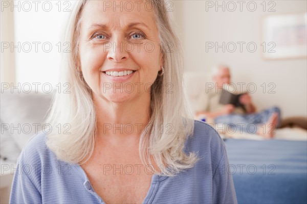 Senior woman smiling with husband reading in background. Photo : Rob Lewine