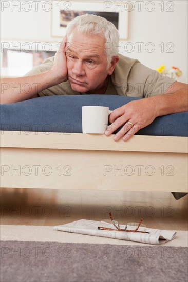 Tired senior man holding coffee cup lying on bed . Photo : Rob Lewine