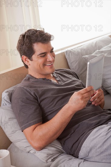 Young man laying on bed and using digital tablet. Photo : Rob Lewine