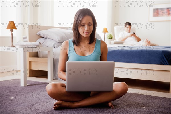 Woman using laptop with husband on lounger in background. Photo : Rob Lewine