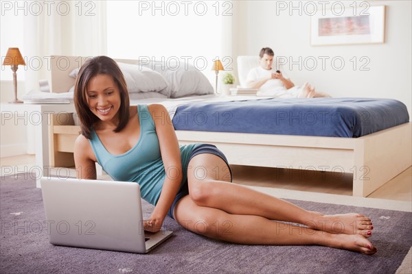 Woman using laptop with husband on lounger in background. Photo : Rob Lewine