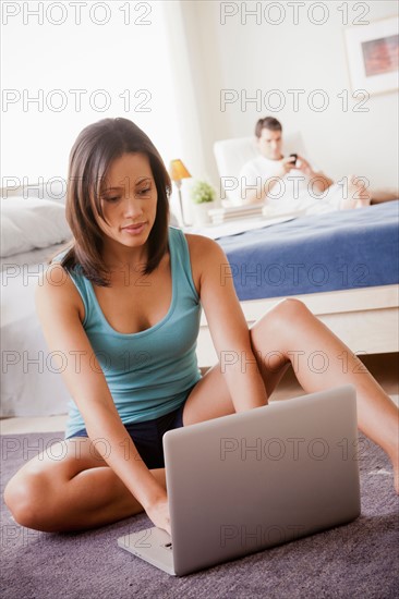 Woman using laptop with husband on lounger in background. Photo : Rob Lewine