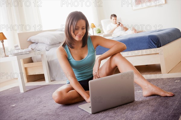 Woman using laptop with husband on lounger in background. Photo : Rob Lewine