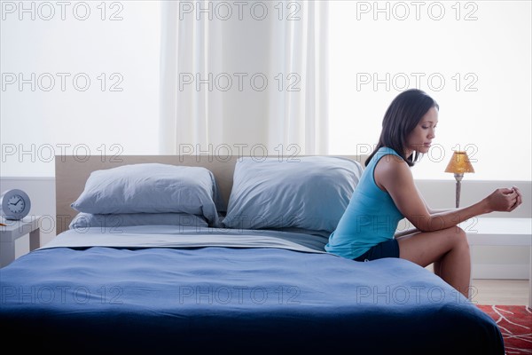 Woman sitting on bed in empty bedroom. Photo : Rob Lewine