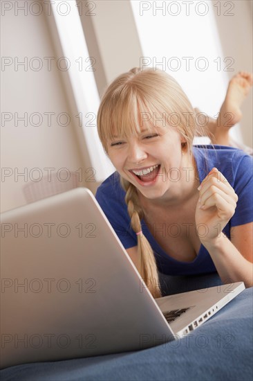 Laughing young woman lying on bed using laptop. Photo: Rob Lewine