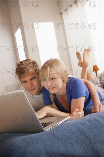 Couple lying on bed using laptop. Photo : Rob Lewine