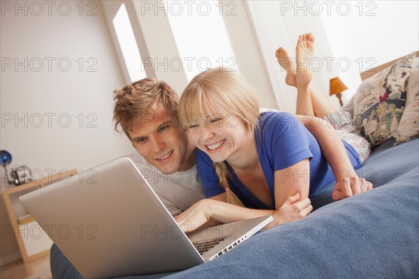 Happy couple lying on bed using laptop. Photo: Rob Lewine