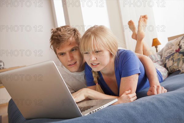 Couple lying on bed using laptop. Photo: Rob Lewine