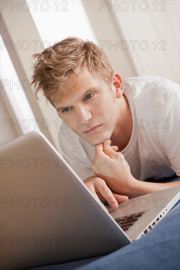 Man lying on bed using laptop. Photo : Rob Lewine