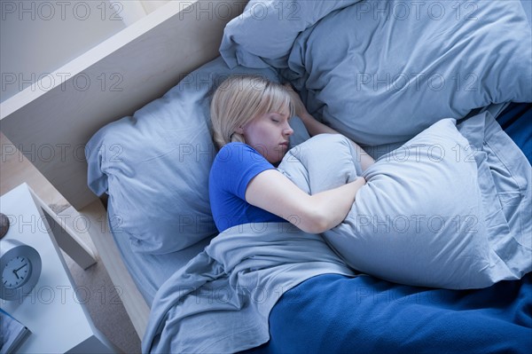 Elevated view of woman sleeping and hugging pillow. Photo : Rob Lewine