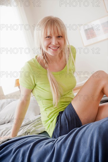 Portrait of smiling young woman sitting on bed. Photo: Rob Lewine