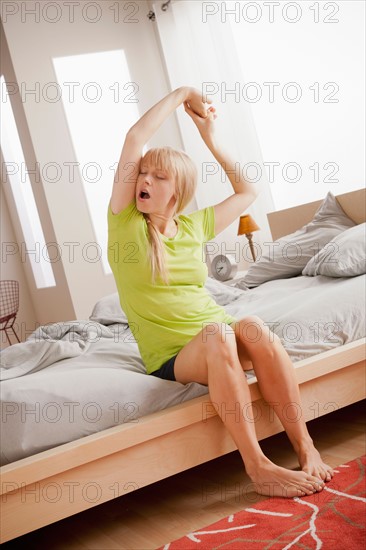 Woman sitting on bed, yawning and stretching. Photo : Rob Lewine