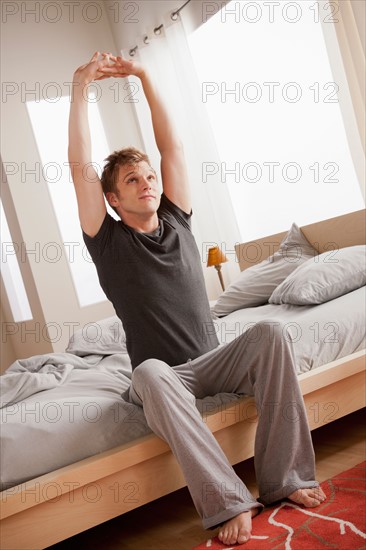 Man sitting on bed and stretching. Photo : Rob Lewine
