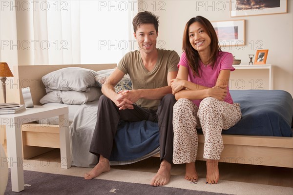 Portrait of couple sitting on bed in nightwear. Photo : Rob Lewine