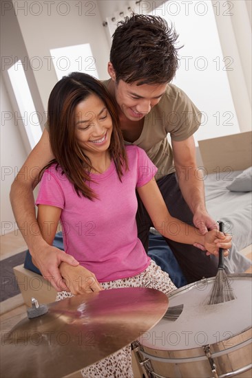 Man teaching woman how to play drums. Photo : Rob Lewine