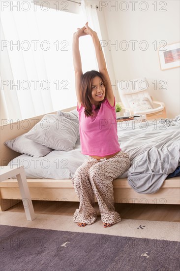 Portrait of woman sitting on bed and stretching her arms. Photo : Rob Lewine