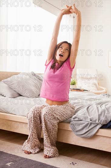 Portrait of woman sitting on bed, stretching her arms and yawning. Photo: Rob Lewine