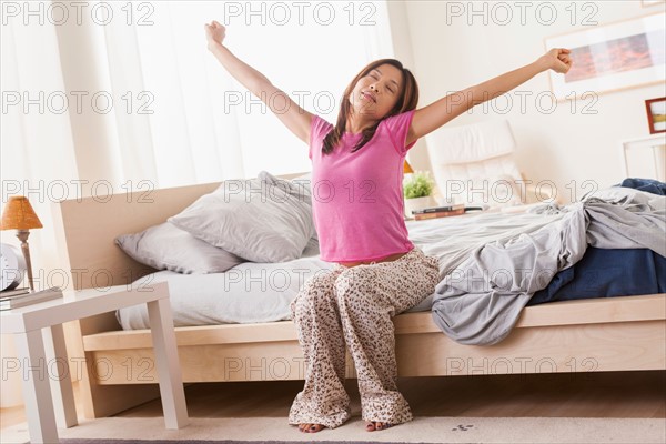 Portrait of woman sitting on bed and stretching her arms. Photo: Rob Lewine