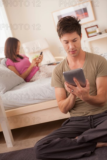 Couple using mobile phone and digital tablet. Photo : Rob Lewine