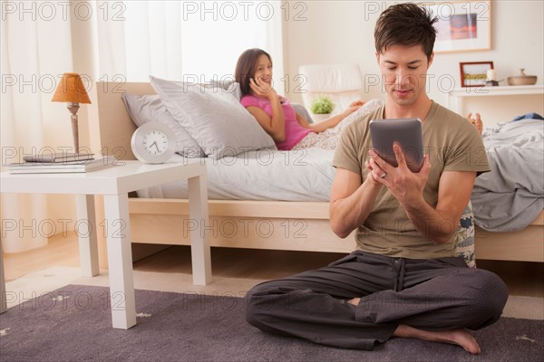 Couple using mobile phone and digital tablet. Photo : Rob Lewine