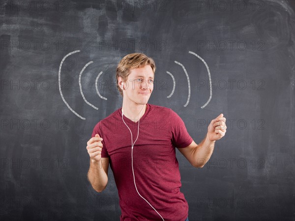 Studio shot of mid adult man listening to music on earphones and dancing with chalk drawing on blackboard. Photo: Jessica Peterson