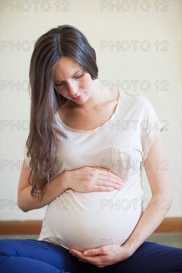 Pregnant mid adult woman looking down and touching her abdomen. Photo : Jessica Peterson