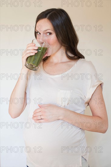 Portrait of pregnant mid adult woman drinking green juice. Photo : Jessica Peterson