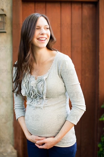 Pregnant mid adult woman standing in front of entrance door. Photo : Jessica Peterson