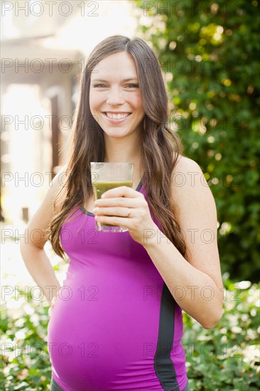Portrait of pregnant mid adult woman in sport clothing holding glass with green juice. Photo : Jessica Peterson