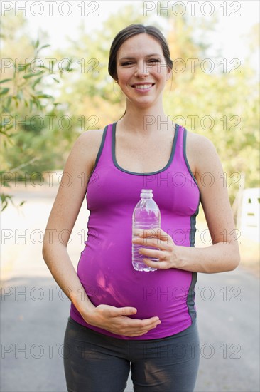 Front view portrait of pregnant mid adult woman in sport clothing holding water bottle. Photo : Jessica Peterson