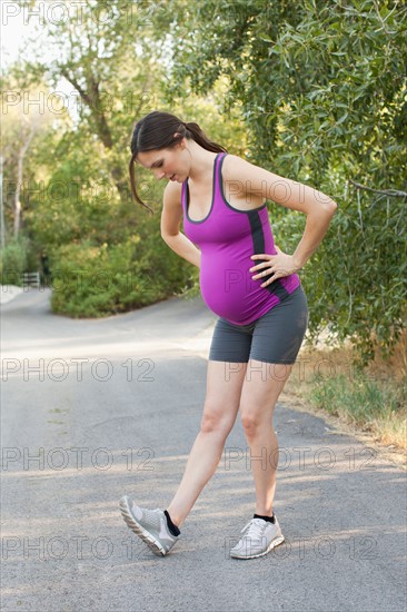 Pregnant mid adult woman in sport clothing stretching legs. Photo : Jessica Peterson