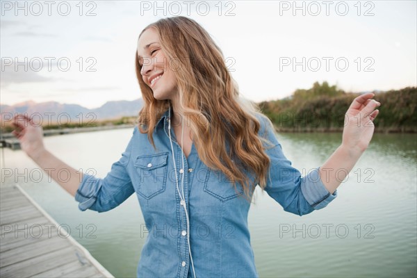 Portrait of young woman listening to mp3 player on jetty. Photo : Jessica Peterson