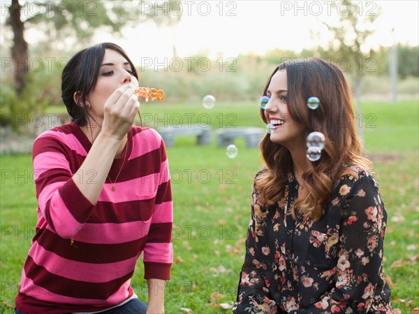 Two young women blowing bubbles in park. Photo : Jessica Peterson