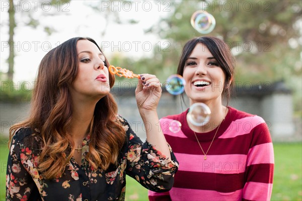 Two young women blowing bubbles in park. Photo: Jessica Peterson