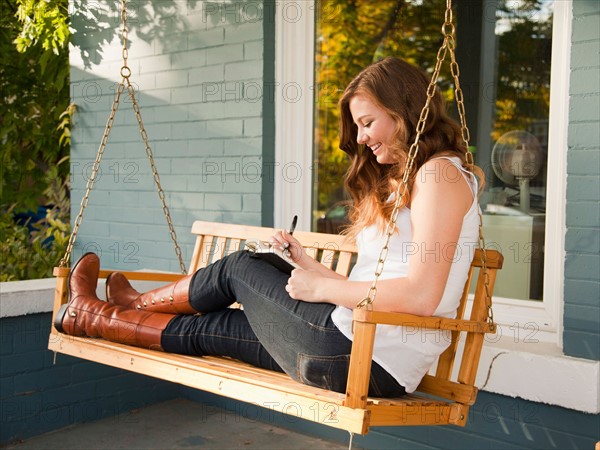 Young woman sitting on swing and making notes. Photo : Jessica Peterson