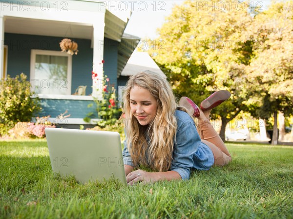 Young woman lying down on grass with her laptop. Photo : Jessica Peterson