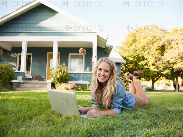 Portrait of young woman lying down on grass with her laptop. Photo : Jessica Peterson