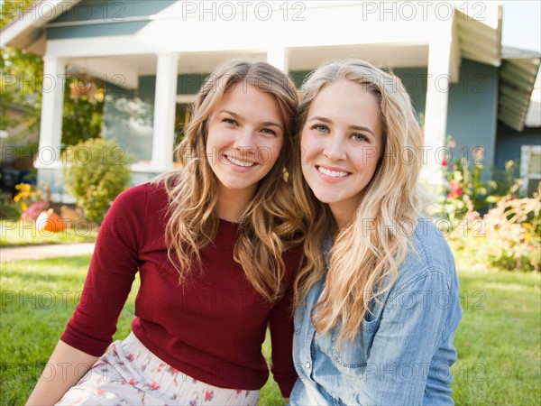 Portrait of two young women cheek to cheek in front of house. Photo : Jessica Peterson