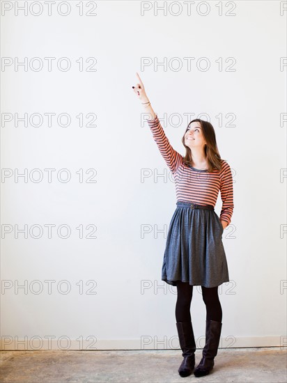 Studio shot young woman looking up and pointing. Photo : Jessica Peterson