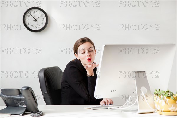 Studio shot of young woman blowing a kiss to computer monitor. Photo : Jessica Peterson