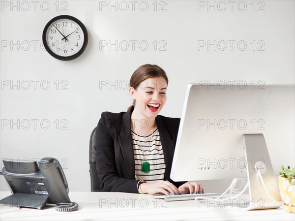 Studio shot of young woman working on computer and laughing. Photo : Jessica Peterson