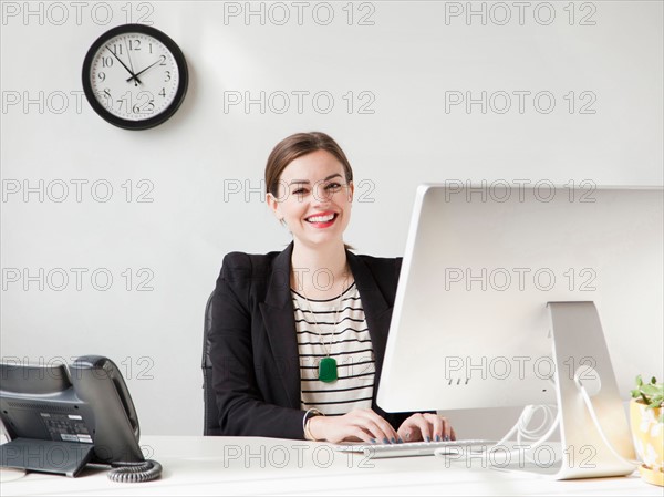 Studio shot portrait of young woman working on computer and smiling. Photo : Jessica Peterson