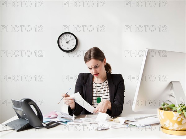 Studio shot of young woman doing paperwork, expressing negativity. Photo : Jessica Peterson