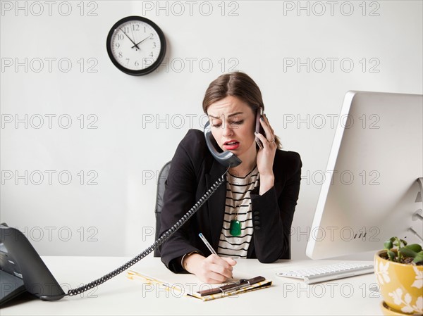 Studio shot of multi-tasking young woman working in office. Photo : Jessica Peterson