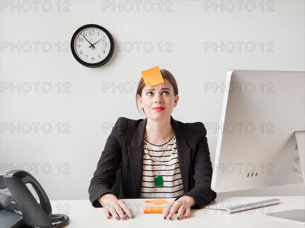 Studio shot of young woman working in office with adhesive note on her forehead. Photo: Jessica Peterson